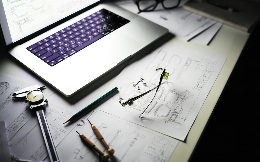 A tablet, technical drawings, dividers and callipers on a desk