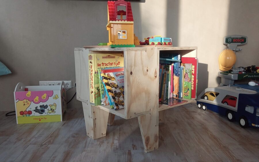 A small plywood book bin in a child's room, front-facing picture books stacked in both open sides