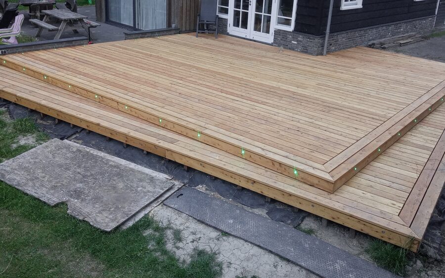A large two-level timber deck against a black-clad house, with small lights set into the edge of the step and along the perimeter