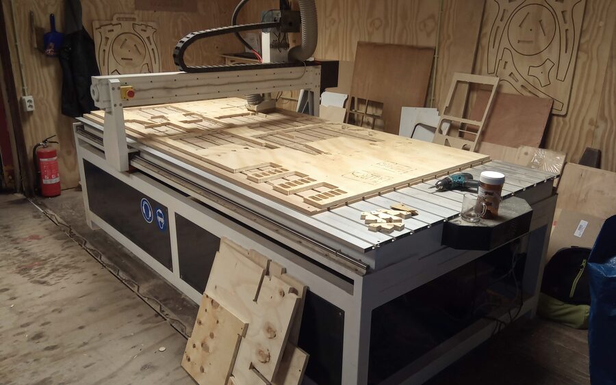 A CNC router with a full sheet of plywood clamped to the bed, parts already cut and nested across it