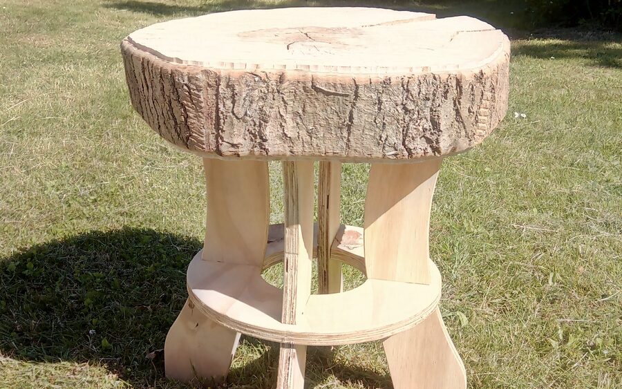 A side table made from a bark-edged log slice resting on curved plywood legs joined by a round stretcher